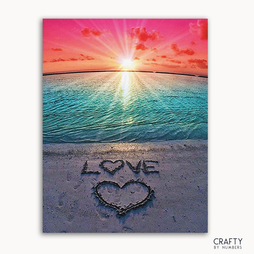 A paint by numbers kit depicting a beach scene with a sunset and the word 'LOVE' written in the sand.