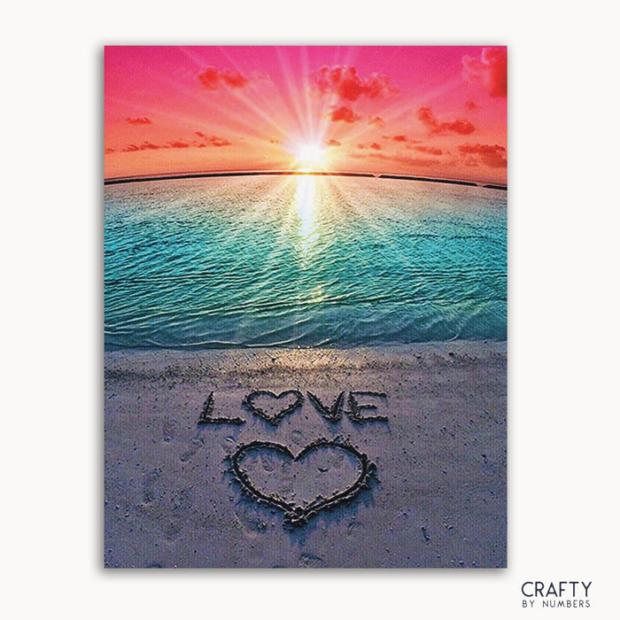 A paint by numbers kit depicting a beach scene with a sunset and the word 'LOVE' written in the sand.