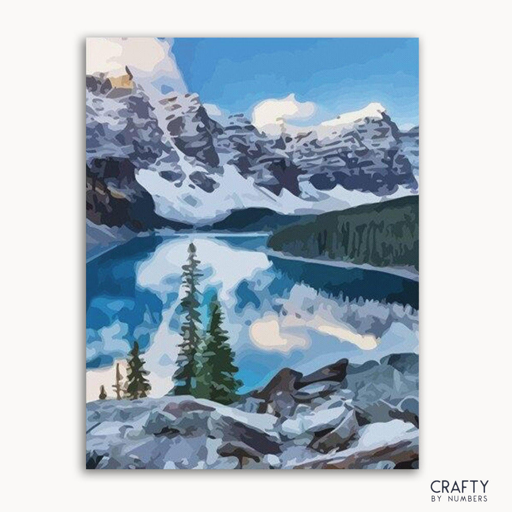 A paint by numbers kit depicting a scenic landscape with a lake and mountains covered in snow.
