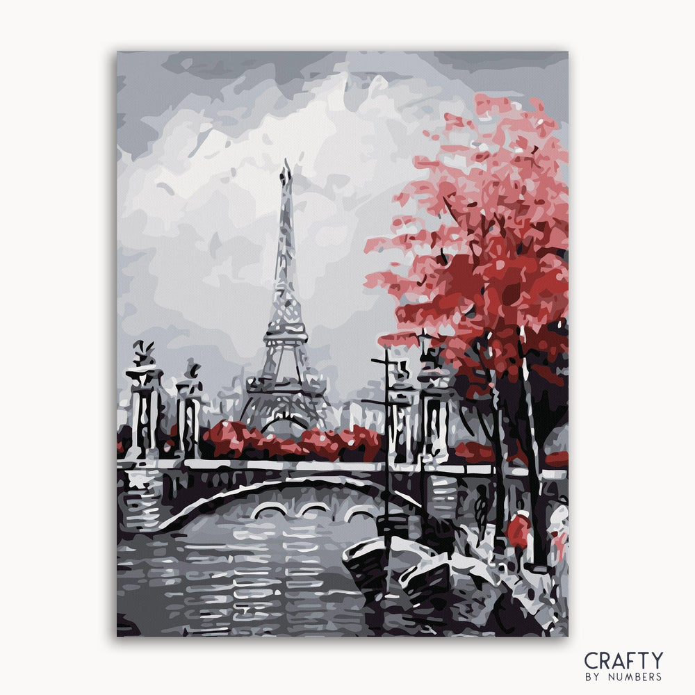A paint-by-numbers kit depicting a landscape with a bridge, river, and a Eiffel Tower-like structure in the background, accompanied by a guide image at the bottom.