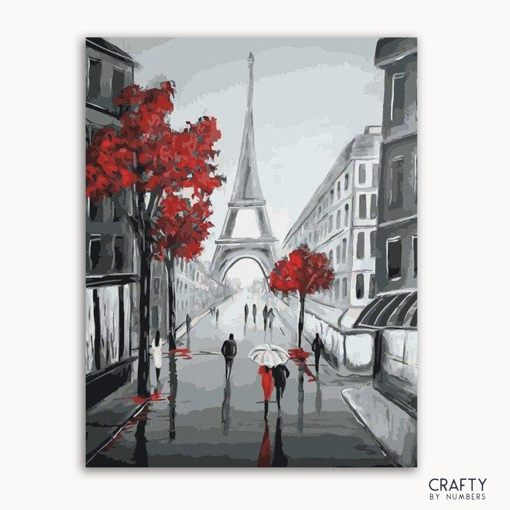 A paint by numbers kit depicting a street scene in Paris with the Eiffel Tower, trees with red leaves, and people walking.