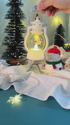 Close-up of glittery holiday ornaments labeled “Ho Ho Holiday Magic,” hanging from evergreen branches with twinkling lights.