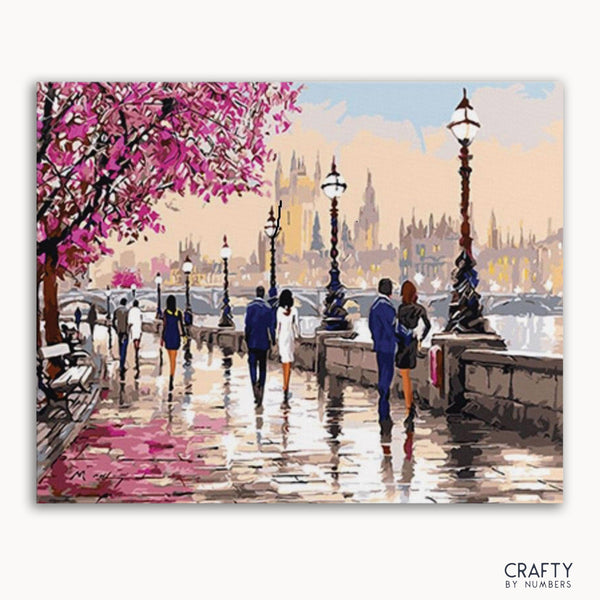 A paint-by-numbers kit depicting a romantic scene with rain in a park in London, with people walking and pink tree blossoms.