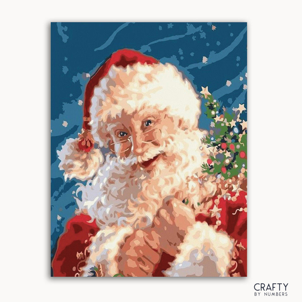 A paint-by-numbers kit depicting Santa Claus with a red hat and white beard, holding a Christmas tree, against a blue background with snowflakes.