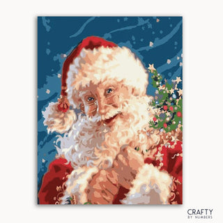 Ein Malen-nach-Zahlen-Set, das den Weihnachtsmann mit rotem Hut und weißem Bart zeigt, der einen Weihnachtsbaum hält, vor einem blauen Hintergrund mit Schneeflocken.