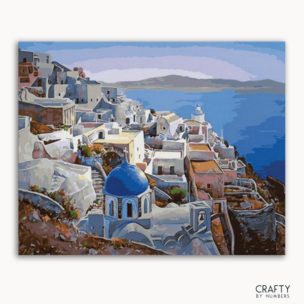 A paint-by-numbers kit depicting a Santorini landscape with white buildings and a blue dome on a canvas, branded by Crafts by Numbers.