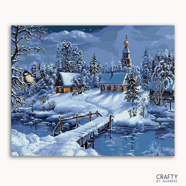 A paint-by-numbers kit depicting a snowy night scenery with a bridge, river, and a village covered in snow.